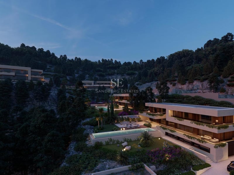 Vue architecturale d'une villa moderne à plusieurs niveaux sur une colline boisée de nuit avec piscine éclairée.