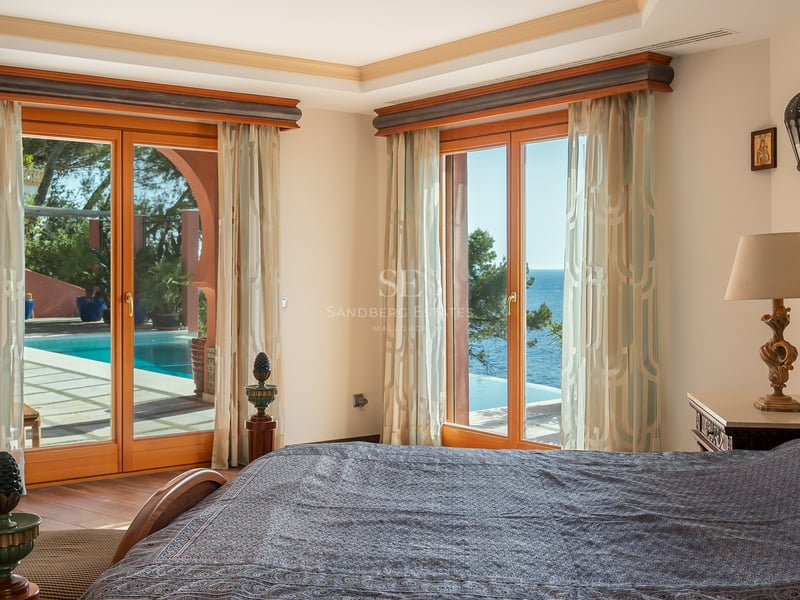Chambre principale avec de grandes fenêtres en bois s'ouvrant sur une terrasse avec piscine et vue sur la mer.