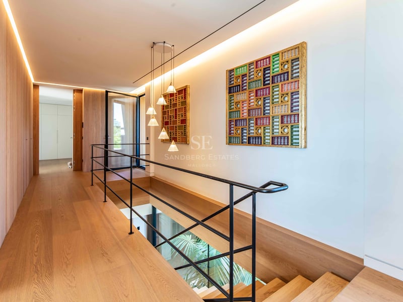 Couloir lumineux avec parquet en chêne, rampe en métal noir et œuvres d'art géométriques colorées.