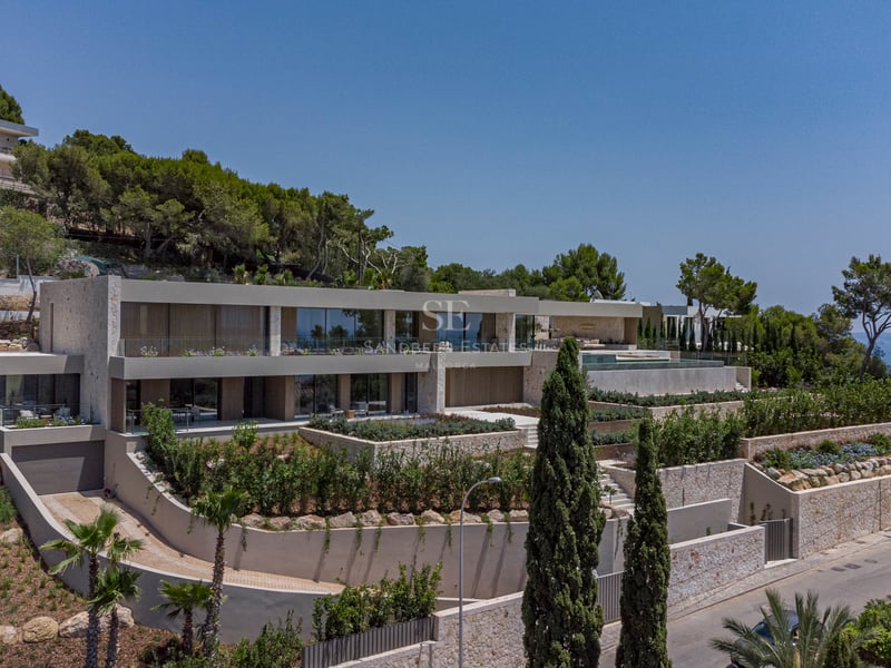 Villa moderne sur plusieurs niveaux sur une colline avec murs en pierre, garde-corps en verre et jardins méditerranéens.