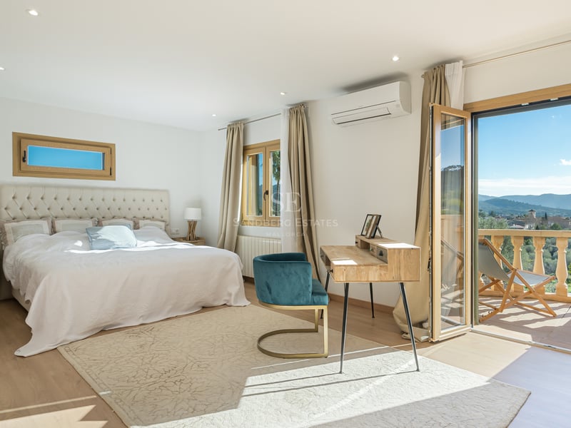 Chambre principale lumineuse avec un grand lit, un bureau en bois et des portes vitrées ouvrant sur un balcon panoramique.