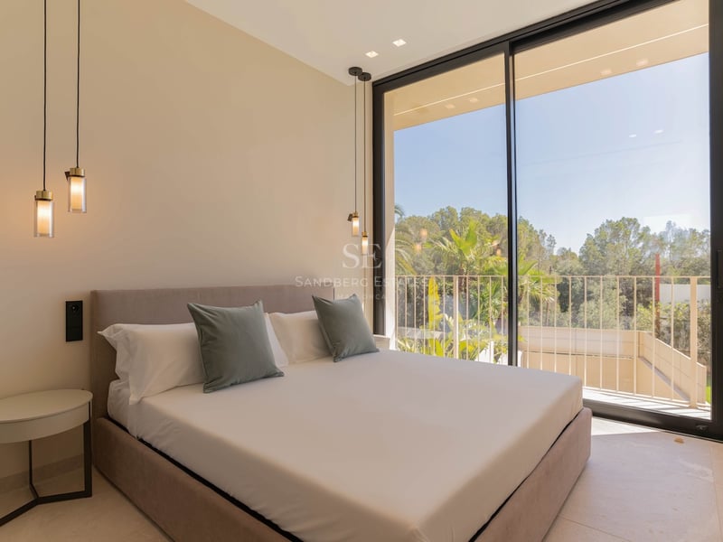Chambre contemporaine avec de grandes baies vitrées, un lit aux tons neutres et une vue sur les arbres.
