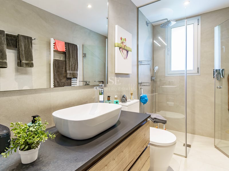 Salle de bain moderne avec vasque à poser blanche, douche vitrée et grand miroir.