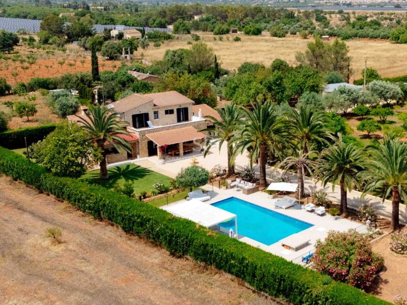 Vue aérienne d'une villa en pierre à deux étages avec piscine bleue, palmiers et grand jardin dans un cadre rural.