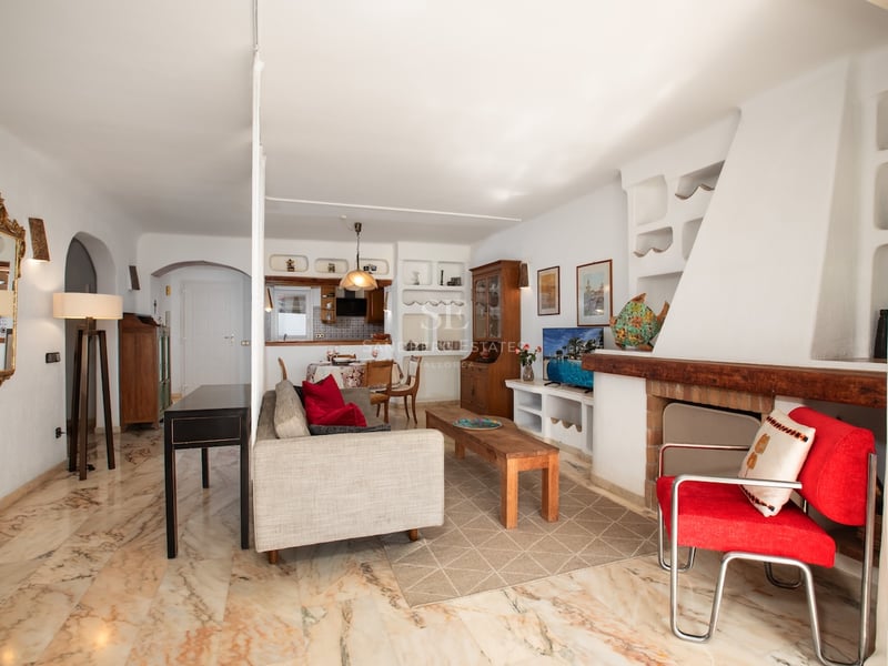 Salon lumineux avec sol en marbre poli, grande cheminée blanche, canapé gris et fauteuil rouge.