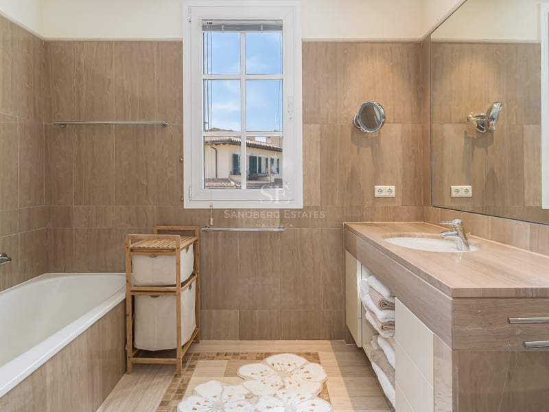 Salle de bain lumineuse avec baignoire, lavabo en pierre, grand miroir et fenêtre offrant une vue urbaine.