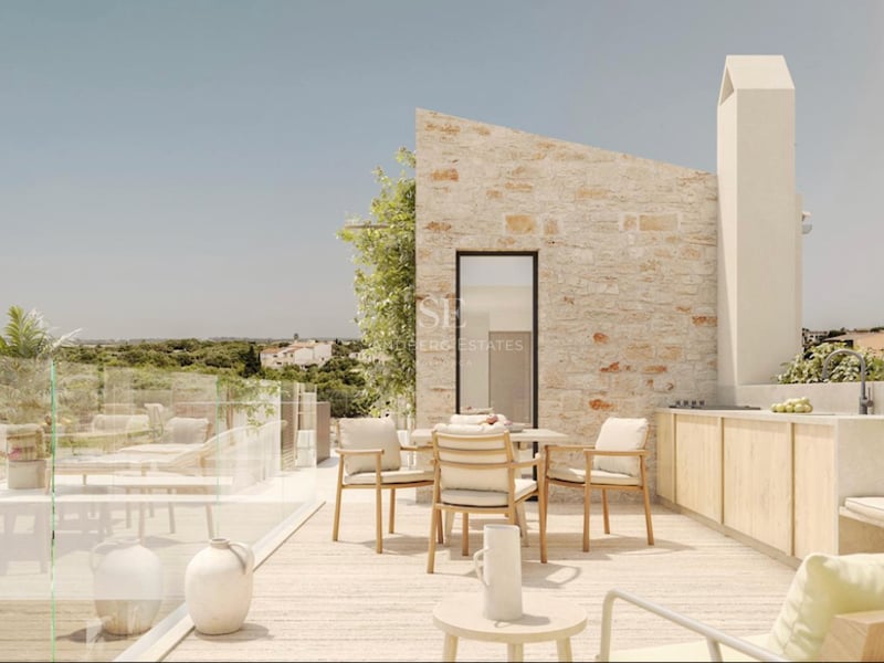 Terrasse moderne en pierre avec coin repas, cuisine extérieure et garde-corps en verre donnant sur la campagne.
