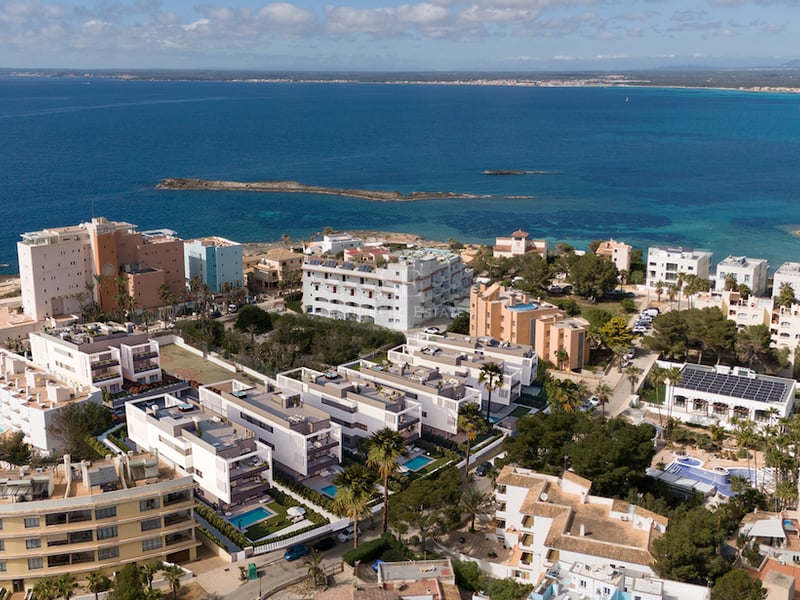 Vista de dron de modernos edificios blancos y piscinas privadas frente al mar Mediterráneo azul intenso.