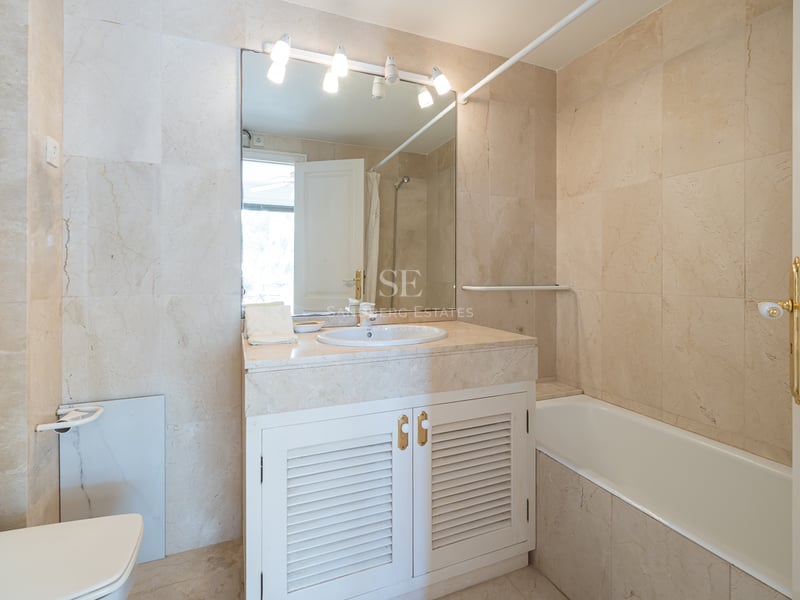 Salle de bains de style méditerranéen avec carrelage en marbre crème, baignoire intégrée et meuble vasque blanc.