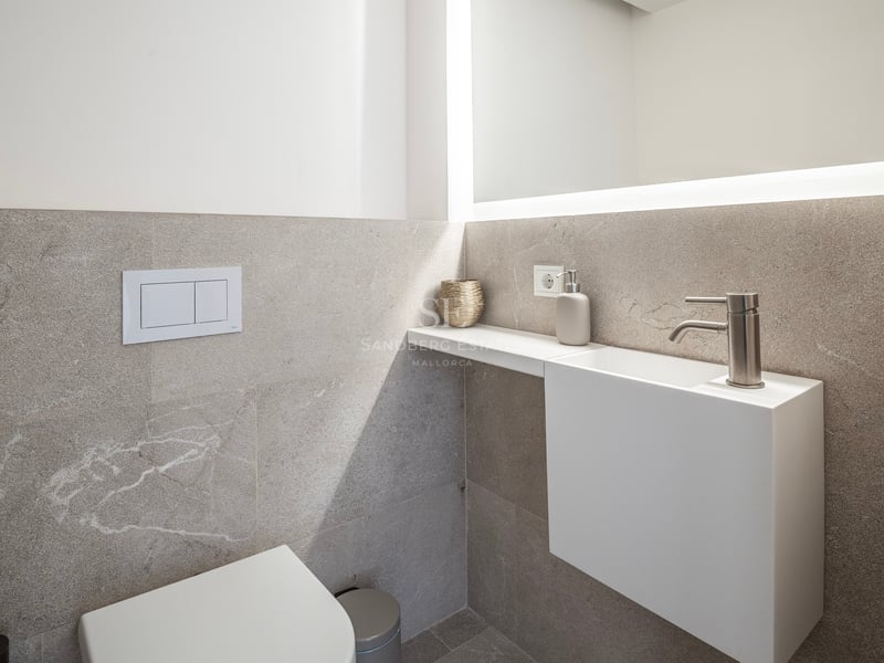 Cabinet de toilette moderne avec carreaux de pierre texturés, lavabo suspendu blanc et grand miroir rétroéclairé.