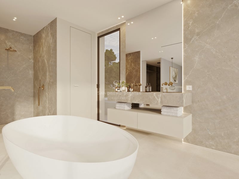 Salle de bain moderne avec baignoire îlot blanche, murs en marbre beige et robinetterie dorée.