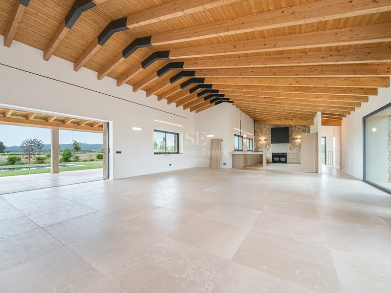 Grand salon moderne avec poutres en bois, sol en pierre et baies vitrées ouvrant sur la piscine et le jardin.