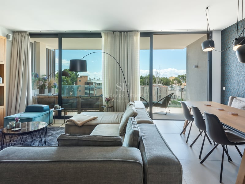 Espace de vie moderne avec canapé gris, salle à manger en bois et grandes baies vitrées menant à une terrasse.