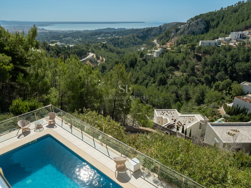 Vue surélevée d'une piscine turquoise sur une terrasse en pierre dominant une vallée verdoyante et la mer.