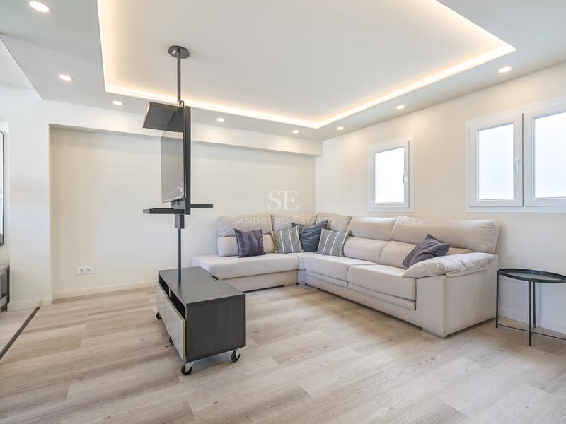 Salon moderne avec grand canapé d'angle beige, parquet clair et support TV pivotant noir minimaliste.