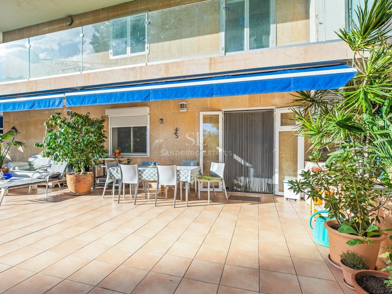 Terrasse ensoleillée avec carrelage, table pour six personnes, stores bleus et balustrades en verre.