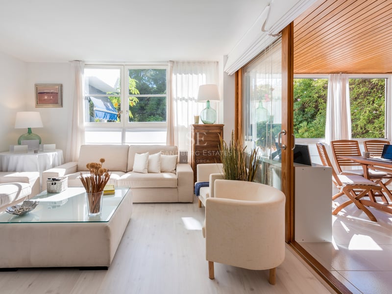 Salon lumineux avec canapés crème et grandes baies vitrées ouvrant sur une terrasse en bois.