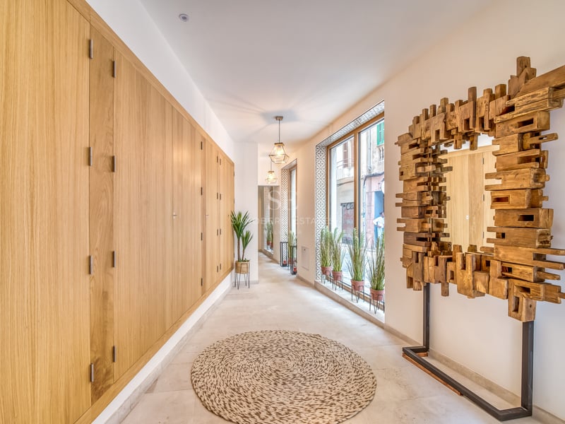 Couloir lumineux avec rangements en chêne du sol au plafond, miroir sculptural en bois et grandes fenêtres.
