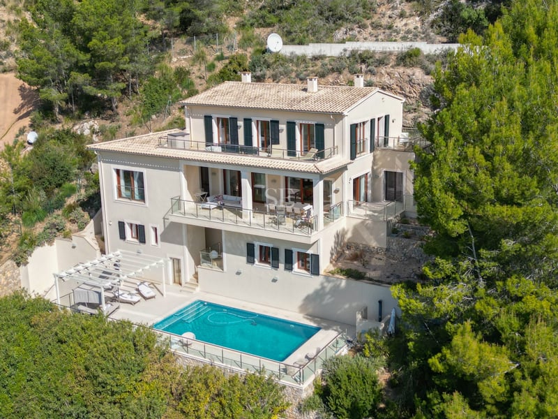 Vue aérienne d'une villa de trois étages avec piscine, terrasses en verre et toit en terre cuite entourée de pins.