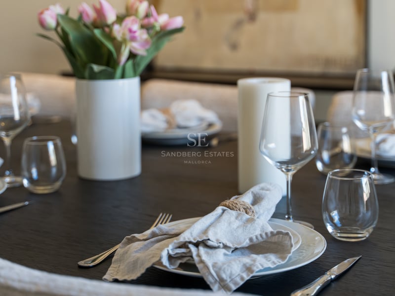 Close-up of a dark wooden dining table set with white plates, linen napkins, crystal glasses, and pink tulips.