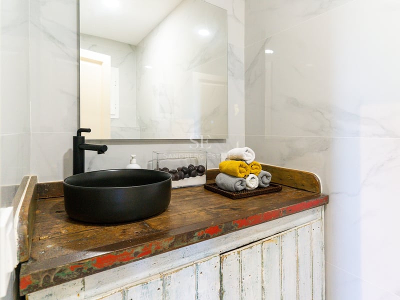 Vasque noir mat sur meuble en bois rustique avec carrelage effet marbre et grand miroir.
