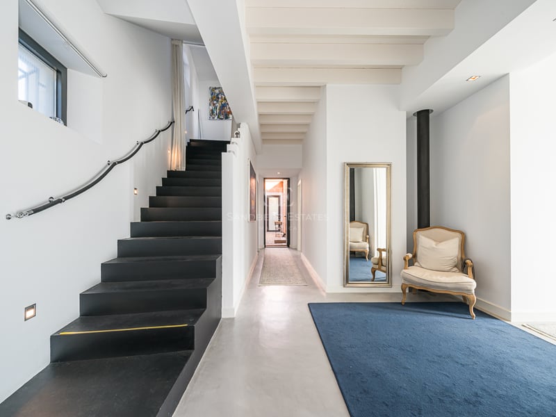 Entrée moderne comprenant un escalier noir élégant, des sols en béton poli et un tapis bleu avec un fauteuil classique.