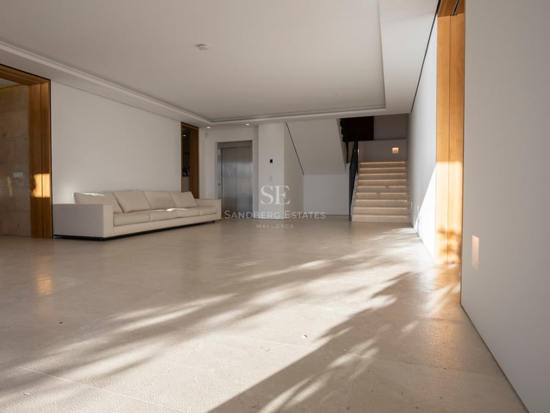 Grand hall minimaliste avec sol en pierre crème, canapé blanc, ascenseur privé et escalier en pierre.