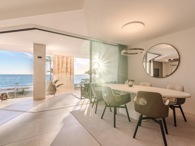 Moderner Essbereich mit ovalem Tisch und Glasschiebetüren, die auf eine sonnige Terrasse am Meer führen.