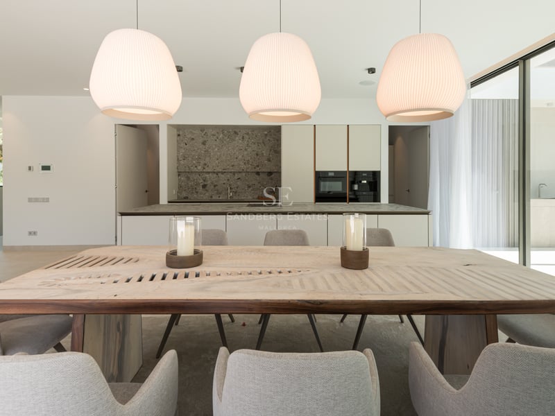 Salle à manger moderne avec table en bois massif, chaises grises et cuisine élégante avec îlot en pierre en arrière-plan.