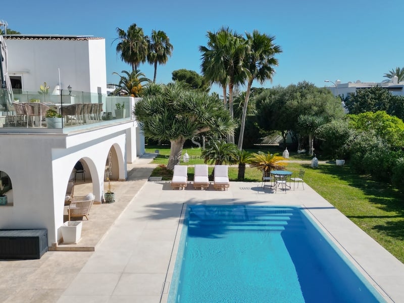 Villa blanche moderne avec piscine rectangulaire bleue, jardin tropical et terrasse avec garde-corps en verre.