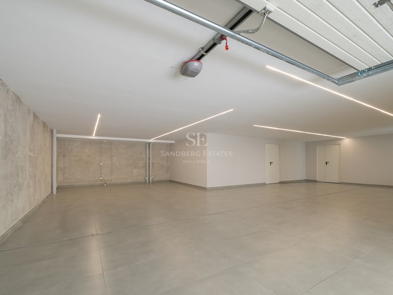 Grand garage souterrain minimaliste avec sol en carrelage gris, murs en béton et éclairage LED linéaire au plafond.
