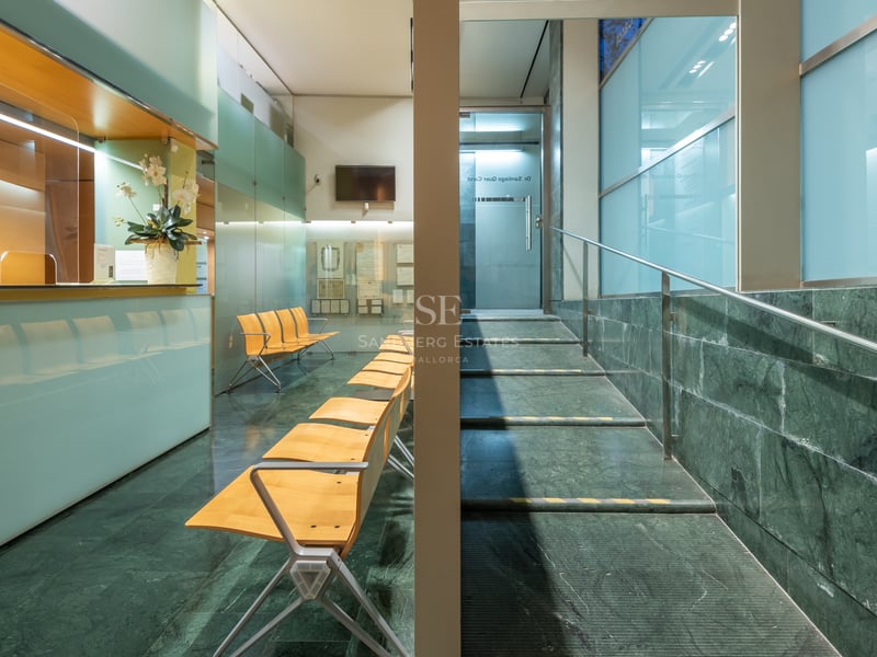 Reception area with green marble flooring, wooden chairs, frosted glass panels, and a staircase with steel handrails.