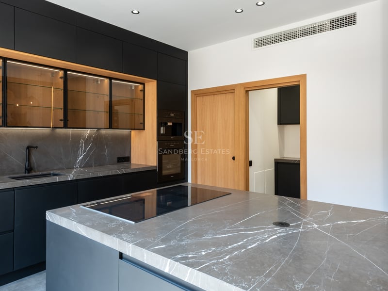 Cuisine moderne avec des armoires noir mat, des plans de travail en marbre gris et des accents en bois.