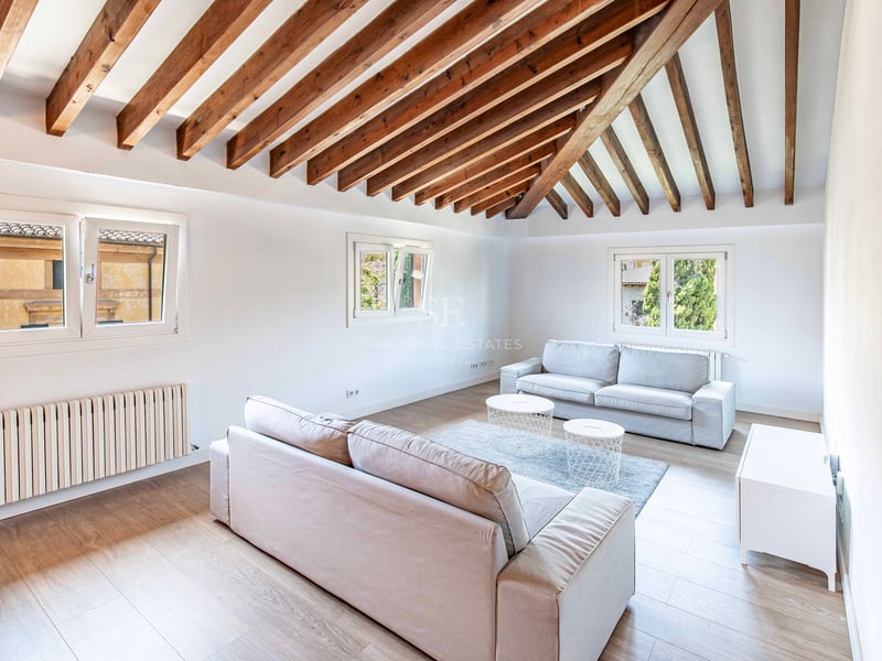 Salon lumineux avec plafond voûté en poutres de bois sombre, canapés neutres et parquet clair.