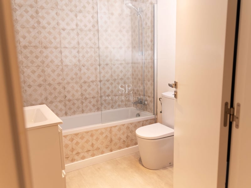 Salle de bain avec carrelage géométrique beige, baignoire avec paroi en verre, toilettes et meuble vasque.