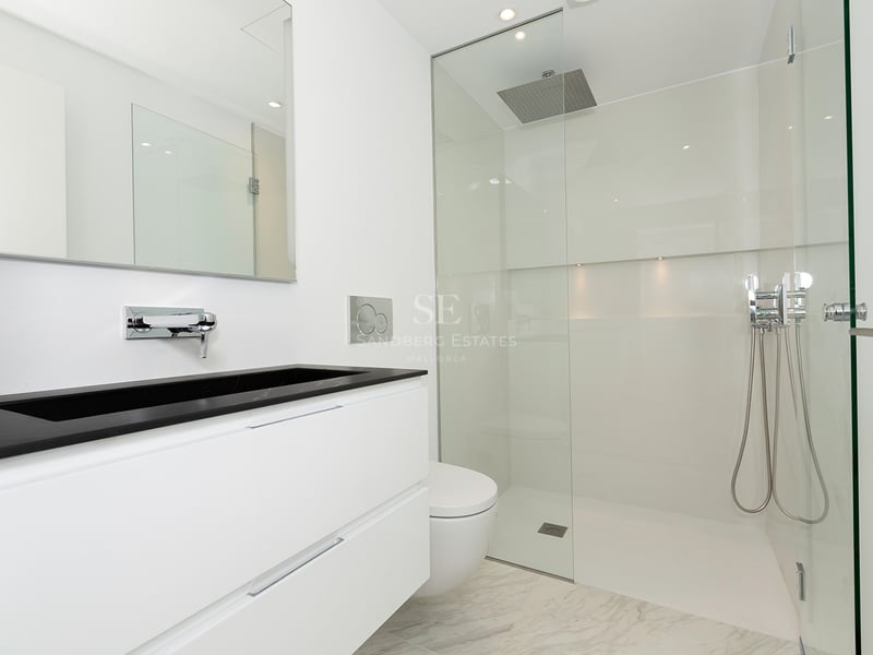 Salle de bains blanche avec douche vitrée, vasque noire intégrée et carrelage effet marbre.