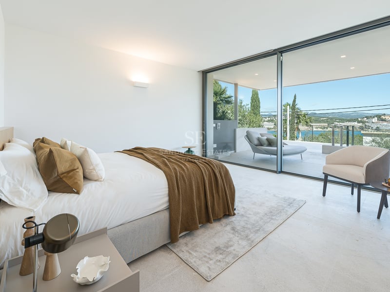 Chambre moderne avec de grandes baies vitrées s'ouvrant sur une terrasse surplombant une ville côtière et la mer.