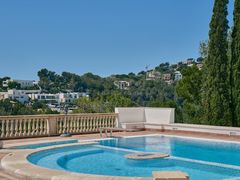 Piscine ensoleillée avec balustrade en pierre et statue classique surplombant une vallée verdoyante et des villas.