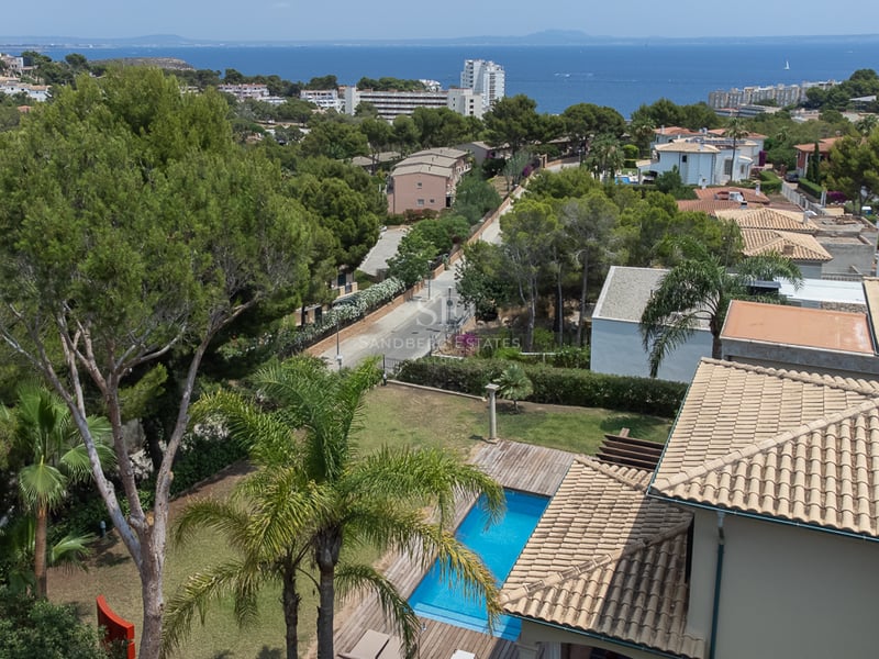 Vue surélevée d'une piscine et de toits en terre cuite avec la mer Méditerranée et la côte à l'horizon.