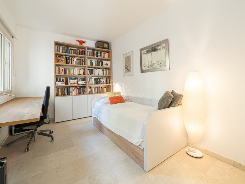 Chambre lumineuse comprenant un lit simple, une grande bibliothèque en bois, un bureau et un lampadaire design.