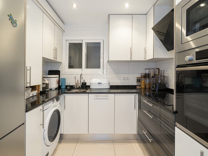 Cuisine moderne en U avec placards blancs, plans de travail noirs et appareils en acier inoxydable.