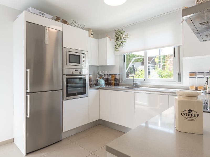 Cuisine moderne lumineuse avec armoires blanches, appareils en inox et porte vitrée donnant sur le jardin.