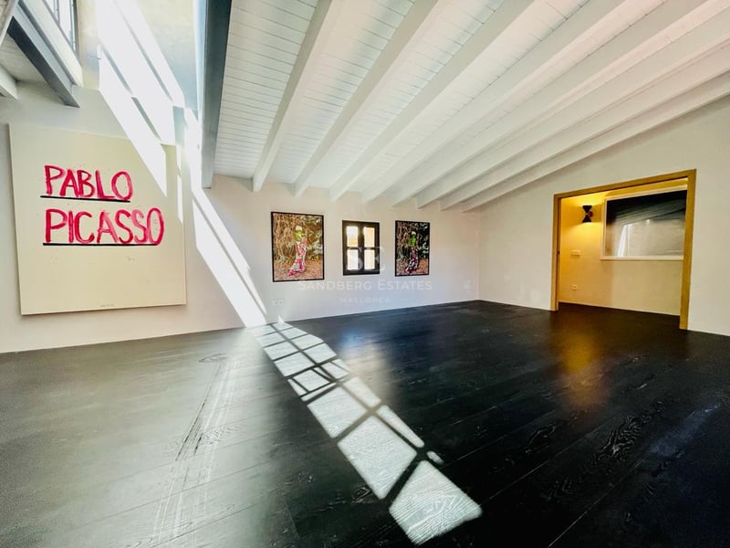 Grande pièce moderne avec parquet foncé, poutres blanches au plafond et une œuvre de Pablo Picasso au mur.