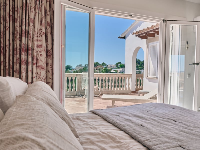 Vue depuis un lit vers une terrasse ensoleillée par des portes vitrées ouvertes avec une balustrade en pierre.