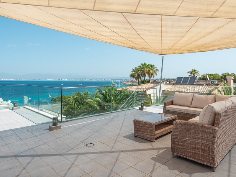 Grande terrasse moderne avec garde-corps en verre, canapés en rotin et voile d'ombrage surplombant la Méditerranée.