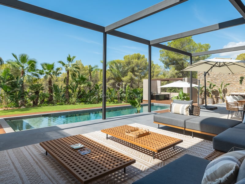 Terrasse moderne avec canapés gris, tables en bois et piscine face à un jardin tropical luxuriant.