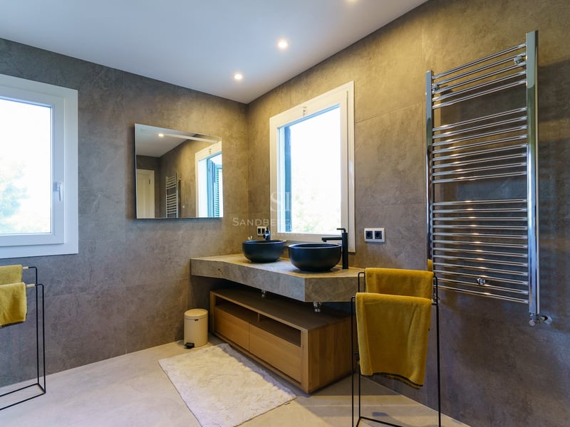 Salle de bain contemporaine avec murs en pierre grise, double vasque noire et grand sèche-serviettes.