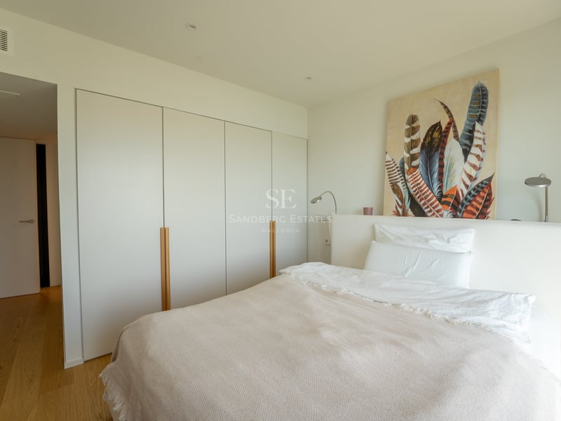 Chambre lumineuse avec lit blanc, grands placards encastrés avec poignées en bois et tableau de plumes.