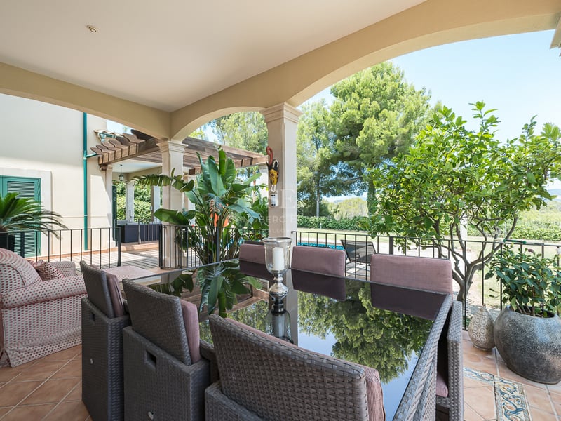 Une terrasse couverte avec un ensemble de salle à manger en rotin, sol en terre cuite et colonnes cintrées.