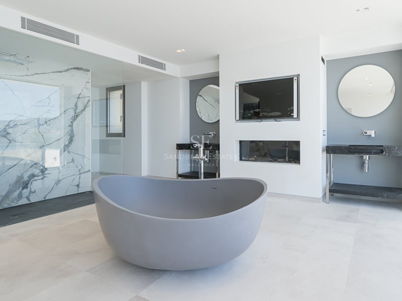 Salle de bain moderne avec baignoire grise, douche en marbre et doubles vasques avec miroirs ronds.
